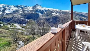 En balkong med utsikt över snöklädda berg, ett träräcke och ett bord med stolar.
