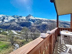 Ein Balkon mit Blick auf schneebedeckte Berge, einem Holgitter und einem Tisch mit Stühlen.