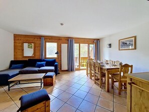A room with a wooden floor, a sofa set, a dining table with chairs, and a large window. - 3rd floor, swimming pool, balcony, tv, ski locker, 58m², Les Menuires (Les Menuires)