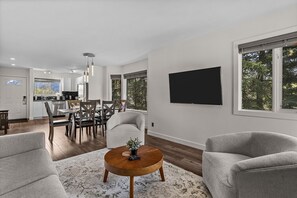 Ein modernes Wohnzimmer mit Essbereich, einem Flachbildfernseher und großen Fenstern.