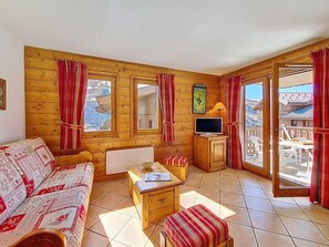 Ein Holzinnenraum mit einer Couch, einem Tisch, einem Fernseher und einem Balkon mit Blick.