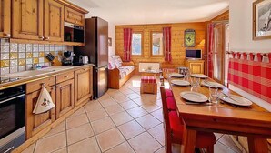 A kitchen with wooden cabinets, a dining table set for four, and a sofa in the background. - 100m from ski slopes, 2nd floor, swimming pool, balcony, tv, ski locker, 50m², Les Menuires (Les Menuires)