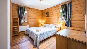 A wooden room with a bed, two bedside lamps, a window with curtains, a radiator, and a wooden cabinet. - 100m from ski slopes, 2nd floor, swimming pool, balcony, tv, ski locker, 50m², Les Menuires (Les Menuires)