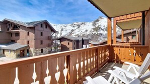 Een balkon met witte stoelen, een houten balustrade met decoratieve details en uitzicht op besneeuwde bergen.