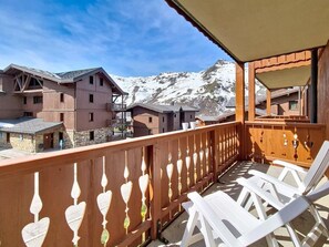 A balcony with white chairs, a wooden railing with decorative elements, and a view of snow-capped mountains. - 2nd floor, swimming pool, balcony, tv, ski locker, 50m², Les Menuires (Les Menuires)