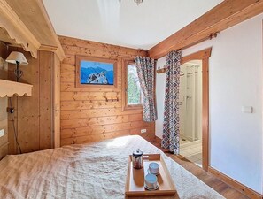 A wooden room with a bed, a painting, a window with patterned curtains, and a shower area visible through an open door. - 2nd floor, swimming pool, balcony, tv, ski locker, 50m², Les Menuires (Les Menuires)