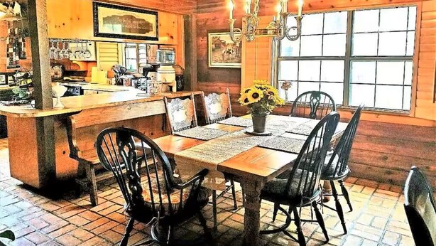 A wooden interior with a dining table, chairs, a chandelier, and a window. - 4B/4B Log Cabin Guesthouse includes an Old Western Town, Saloon & Firepit! (Cleburne)