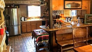 A wooden interior with a kitchen area, a dining table, and a bench. - 4B/4B Log Cabin Guesthouse includes an Old Western Town, Saloon & Firepit! (Cleburne)