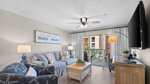 Ein Wohnzimmer mit Sofa, Couchtisch und Fernseher. An der Wand befindet sich ein Schild mit der Aufschrift 'Welcome to the Beach House'.