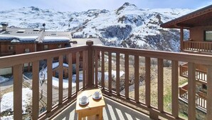 Een houten balkon met een tafel en stoelen, met uitzicht op een besneeerd berglandschap.