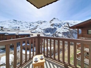 Ein Holzbalkon mit Tisch und Stühlen mit Blick auf eine verschneite Berglandschaft.