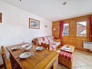 Ein Holzespeisetisch mit Tellern und Gl äsern, ein Sofa mit gemustertem Bezug und ein Fenster mit Vorhängen.