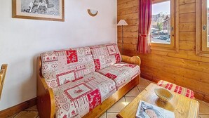 Een gezellige kamer met een gestreept sofa, een ingelijst schilderij aan de muur, een raam met gordijnen en een klein tafeltje met een mand.