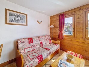 Ein gemütliches Zimmer mit einer gemusterten Couch, einem gerahmten Bild an der Wand, einem Fenster mit Vorhängen und einem kleinen Tisch mit einem Korb.
