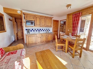 Eine gemütliche Küche mit Holzschränken, einer Mikrowelle und einer gefliesten Spritzschutzwand. Es gibt eine Essecke mit einem Holztisch und Stühlen, sowie ein Sofa mit gemustertem Bezug.