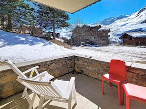 Eine Terrasse mit einem Steinkamin, weißen und roten Stühlen und Blick auf schneebedeckte Berge.