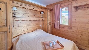 Quarto de madeira com cama, janela com cortinas e bandeja com xícaras e uma colher sobre a cama.