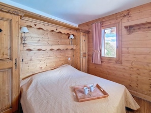 Ein Zimmer aus Holz mit einem Bett, einem Fenster mit Vorhängen und einem Tablett mit Tassen und einem Löffel auf dem Bett.