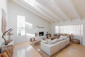 Een ruime woonkamer met een witte bank, een open haard en een eethoek.