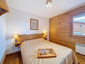 A bedroom with a wooden headboard, a bedside table with a lamp, a window with a view, and a tray with cups and a pot on the bed. - Floor -1, swimming pool, terrace, tv, ski locker, 32m², Les Menuires (Les Menuires)