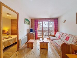 A room with a bed, a sofa, a small table, a TV, and a balcony with a view. - Floor -1, swimming pool, terrace, tv, ski locker, 32m², Les Menuires (Les Menuires)