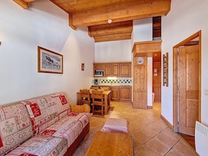 A cozy living room with a sofa, a dining table, and a kitchen area with wooden cabinets and a tiled backsplash. - 3rd floor, swimming pool, balcony, tv, ski locker, 32m², Les Menuires (Les Menuires)