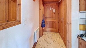Un couloir étroit aux murs et aux portes en bois, avec un sol carrelé et un sac bleu accroché au mur.