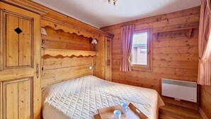 Une pièce en bois avec un lit, une fenêtre avec des rideaux, un radiateur fixé au mur et un plateau avec des tasses posé sur le lit.