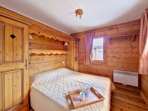 Ein Zimmer mit Holzboden, einem Bett, einem Fenster mit Vorhängen, einem Wandheizkörper und einem Tablett mit Tassen auf dem Bett.