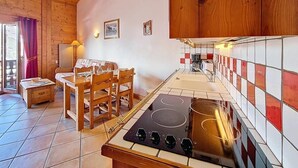 Een keuken met houten kastjes, een fornuis, een eettafel met stoelen en een bijzettafeltje met een lamp.