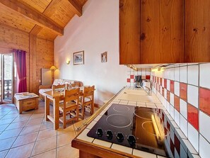 A kitchen with wooden cabinets, a stove, a dining table with chairs, and a small table with a lamp. - 100m from ski slopes, 2nd floor, swimming pool, terrace, tv, ski locker, 32m², Les Menuires (Les Menuires)