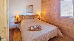 Een kamer met houten vloer, een bed, nachtkastje, een ingelijste foto en een raam.