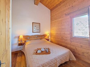 A wooden room with a bed, a nightstand, a framed picture, and a window. - 100m from ski slopes, 2nd floor, swimming pool, terrace, tv, ski locker, 32m², Les Menuires (Les Menuires)