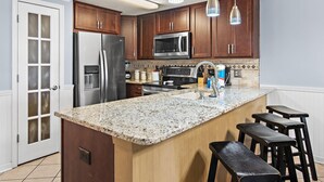 Cocina con gabinetes de madera, electrodomésticos de acero inoxidable, encimera de granito e iluminación colgante.