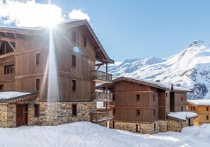 Eine Holzlodge mit mehreren Balkonen und einem Steinfundament, vor einer verschneiten Berglandschaft.