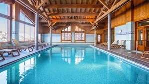 Ett poolområde med träbjälkar, solstolar och stora fönster.
