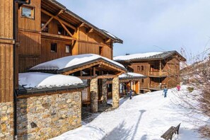 A wooden chalet with stone walls, a covered porch, and a snowy landscape. - 100m from ski slopes, Ground floor, swimming pool, balcony, tv, ski locker, 32m², Les Menuires (Les Menuires)
