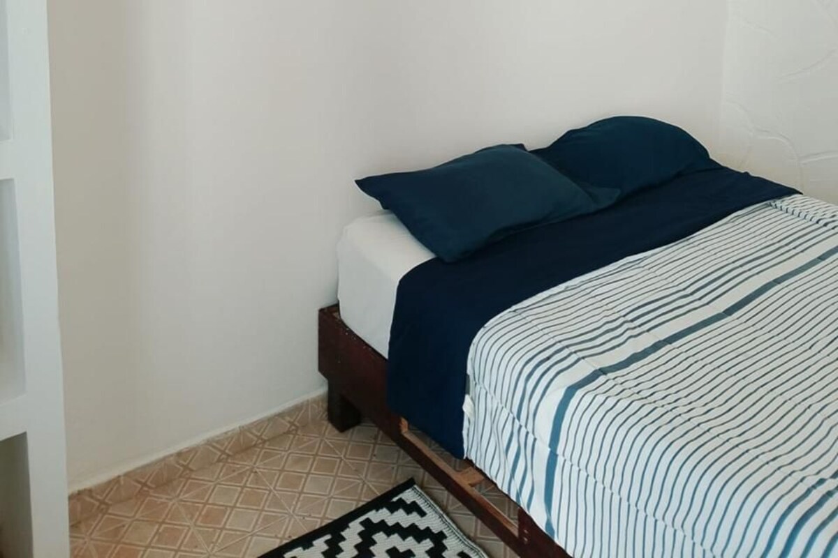 A bedroom with a bed, a patterned rug, and wall-mounted decor.