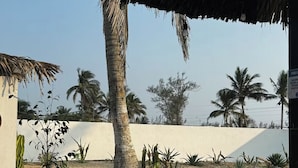 Un salón junto a la playa con techo de paja, un sofá con cojines estampados anaranjados y palmeras al fondo.