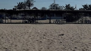 Una playa arenosa con un edificio pequeño, posiblemente un hotel, al fondo.