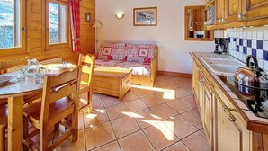 Interior de una cabaña de madera con una mesa de comedor, sillas, un sofá y una zona de cocina.