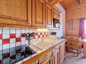 A kitchen with wooden cabinets, a tiled backsplash, a sink, and a dining area with wooden chairs and a table. - 3rd floor, swimming pool, balcony, tv, ski locker, 40m², Les Menuires (Les Menuires)