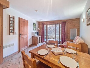 A dining area with a wooden table set for four, a sofa, a TV, and a window with curtains. - Floor -1, swimming pool, terrace, tv, ski locker, 32m², Les Menuires (Les Menuires)