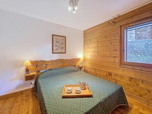 A wooden-paneled room with a bed, two bedside lamps, a framed picture on the wall, and a window with a view. - Floor -1, swimming pool, terrace, tv, ski locker, 32m², Les Menuires (Les Menuires)