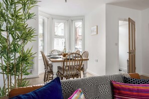 A living room with a sofa, a dining table with chairs, a large plant, and a door leading to another room. - Porto Bello - spacious home with sunny patio (Poole)