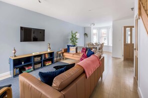 A living room with a sofa, a TV, a bookshelf, and a dining area with chairs and a table. - Porto Bello - spacious home with sunny patio (Poole)