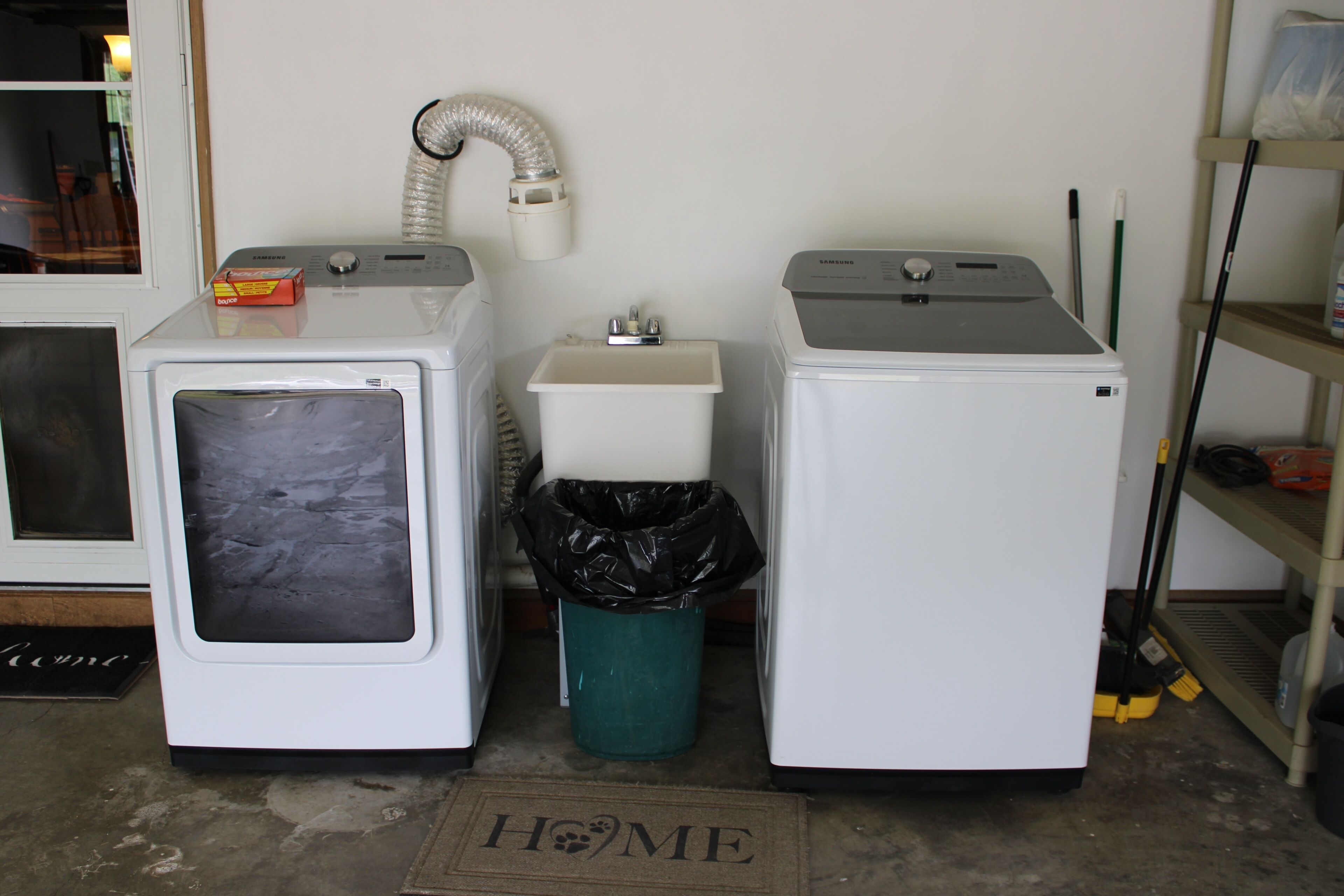 A laundry area with two washing machines, a sink, and a trash can.