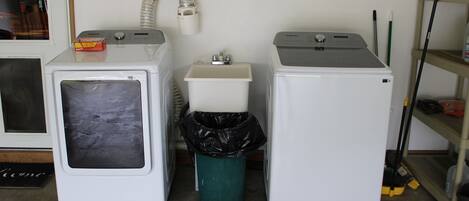 A laundry area with two washing machines, a sink, and a trash can.