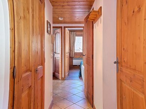 A wooden hallway with a tiled floor, wooden doors, and a window with curtains. - Ground floor, swimming pool, balcony, tv, ski locker, 32m², Les Menuires (Les Menuires)