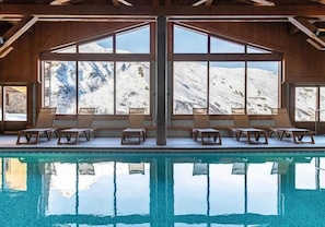 A pool with lounge chairs and large windows offering a mountain view. - Ground floor, swimming pool, balcony, tv, ski locker, 32m², Les Menuires (Les Menuires)